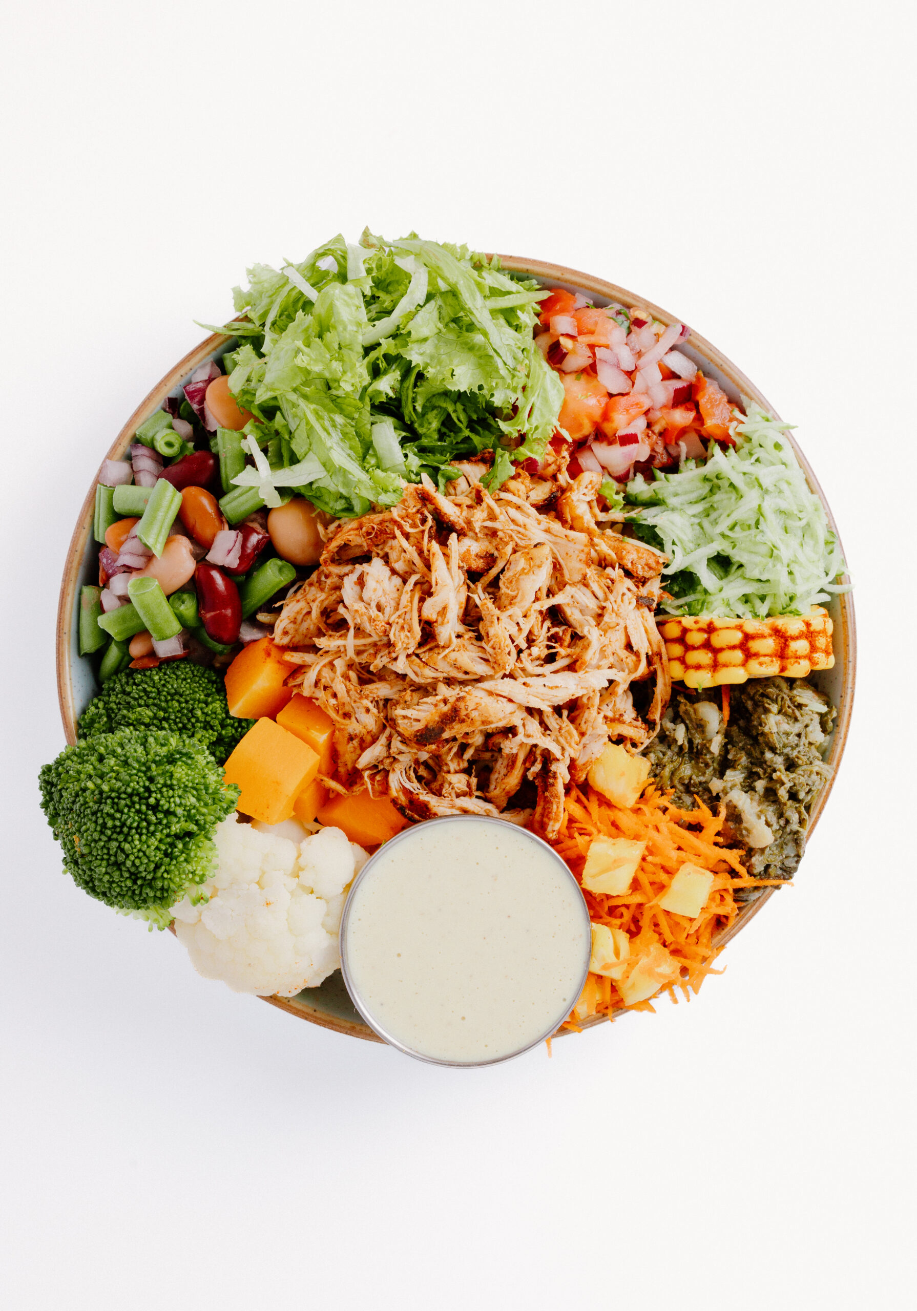 ON chicken and vegetable bowl with fresh salad, broccoli, cauliflower, corn and a side of dressing.